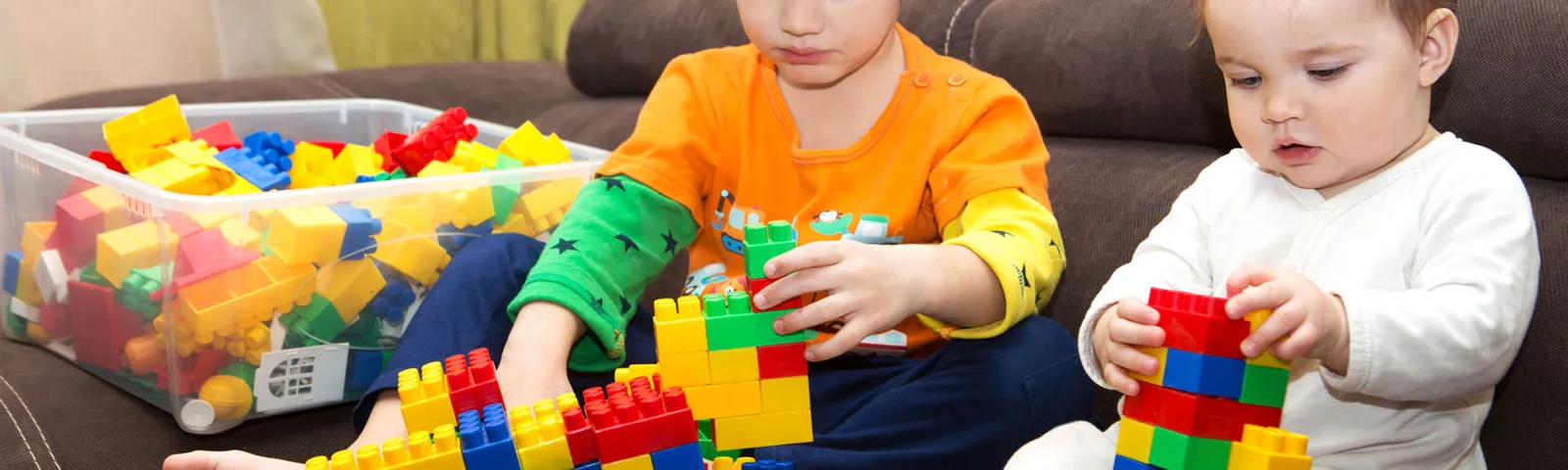 baby and young child playing with toy on a couch