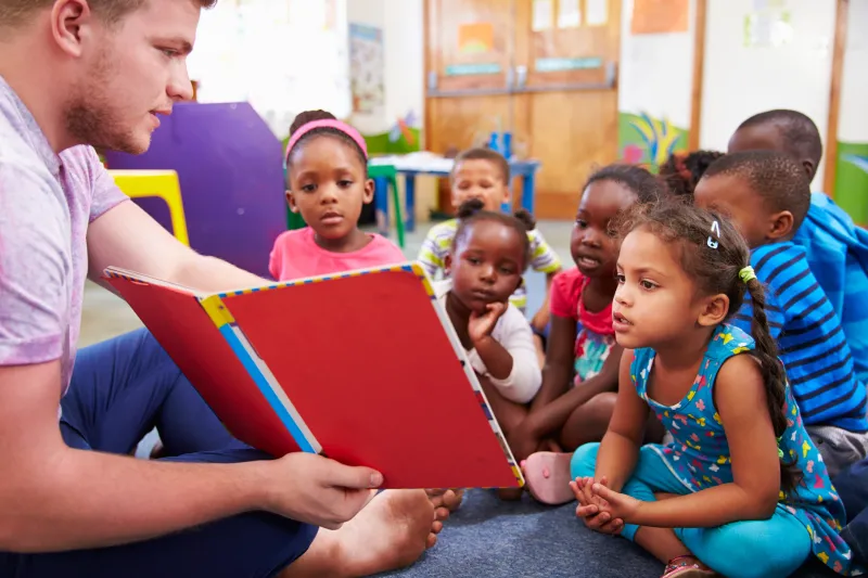 Volunteer teacher reading to a class of preschool kids stock photo