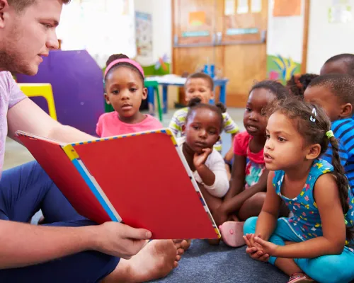 Volunteer teacher reading to a class of preschool kids stock photo